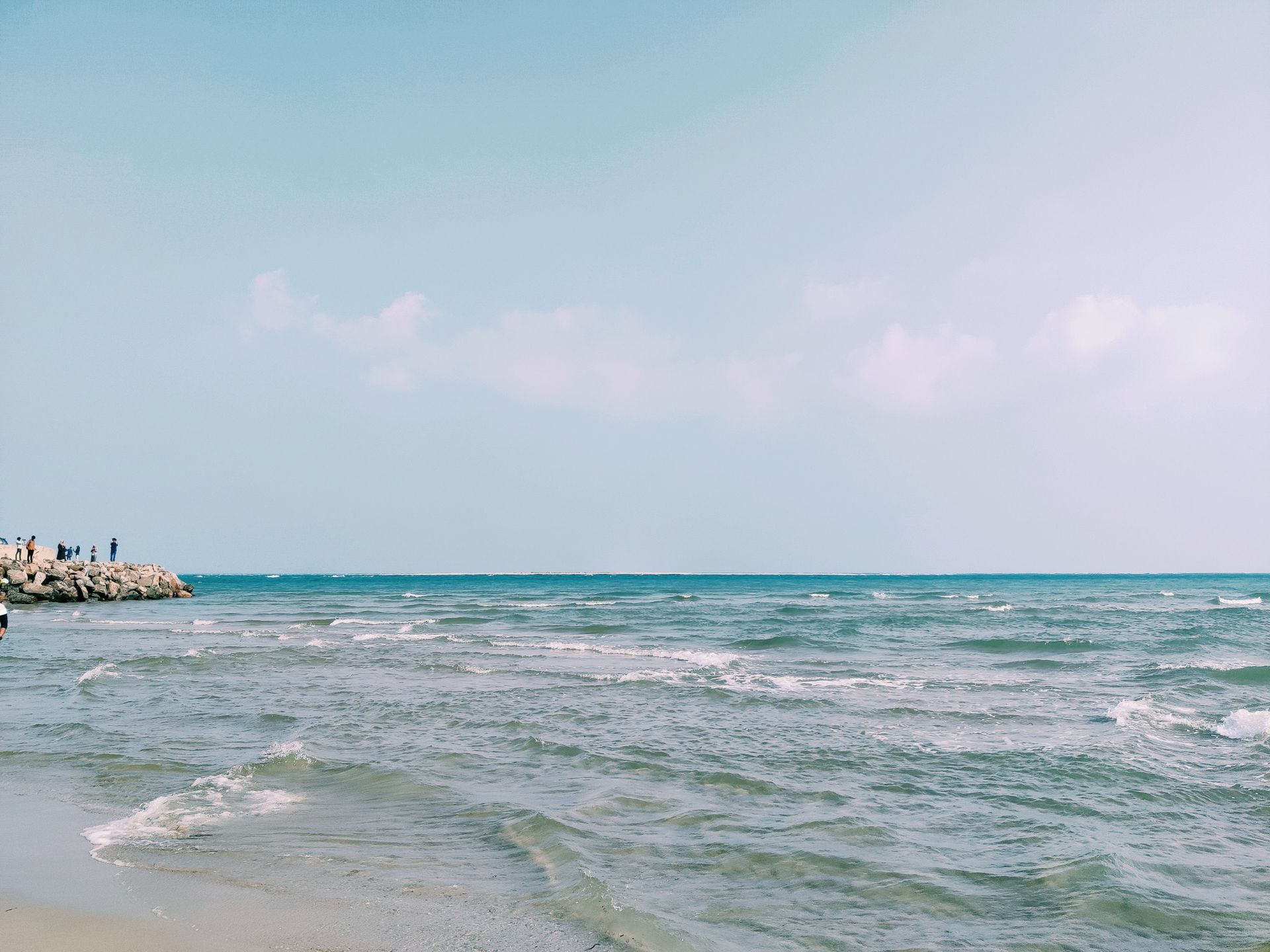 O mar de dia, com a linha do horizonte ao fundo e a espuma chegando na areia